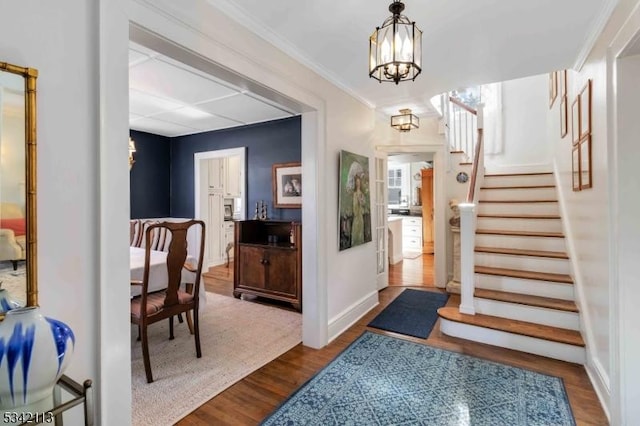 foyer entrance with wood finished floors, baseboards, stairs, an inviting chandelier, and crown molding