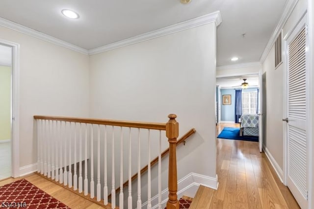 hall with wood finished floors, baseboards, an upstairs landing, and ornamental molding