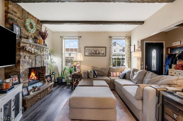 living room with beam ceiling, a stone fireplace, and wood finished floors