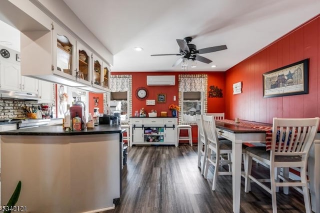 kitchen featuring dark wood-style flooring, dark countertops, white cabinets, a wall mounted air conditioner, and under cabinet range hood