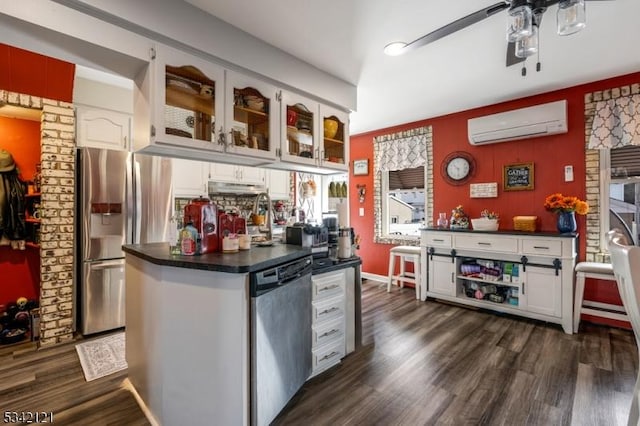 kitchen with dark wood-style floors, dark countertops, appliances with stainless steel finishes, an AC wall unit, and white cabinetry