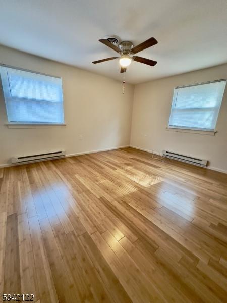 unfurnished room with a baseboard radiator, baseboards, ceiling fan, and wood finished floors