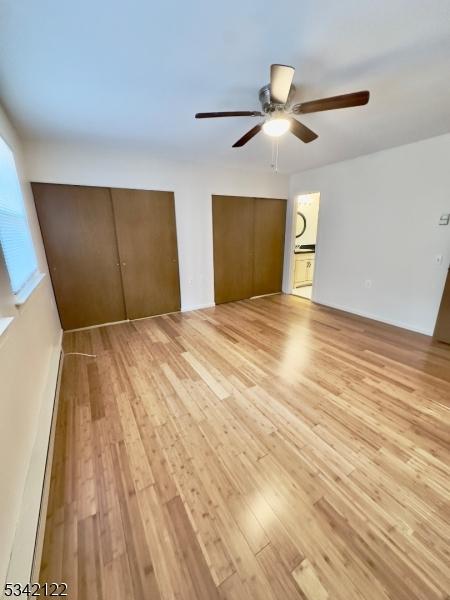 unfurnished bedroom featuring ceiling fan, light wood-type flooring, and multiple closets