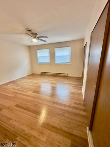 spare room featuring a baseboard heating unit, ceiling fan, light wood-style flooring, and baseboards