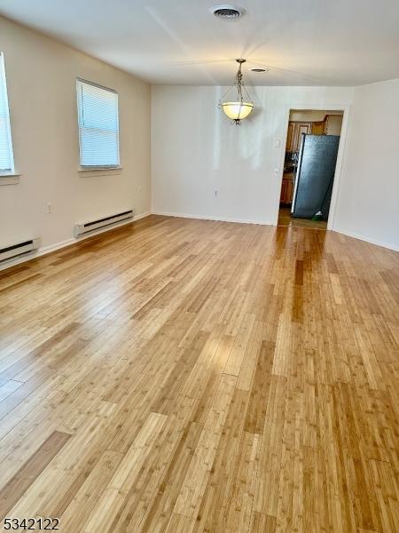 interior space with baseboard heating, light wood-type flooring, and visible vents