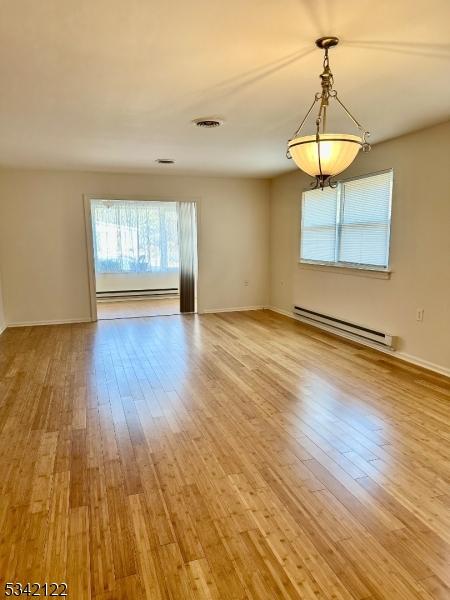 empty room featuring a baseboard heating unit, a baseboard radiator, visible vents, and wood finished floors