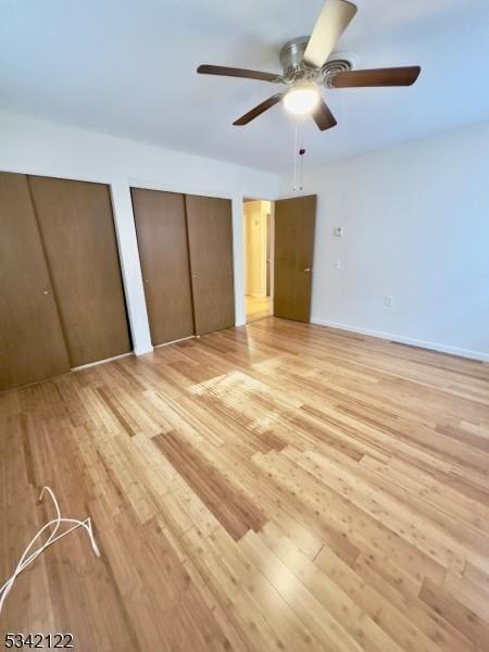 unfurnished bedroom with light wood-style floors, a ceiling fan, baseboards, and two closets