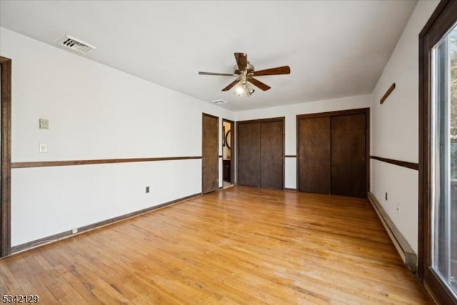 unfurnished bedroom with a baseboard radiator, visible vents, baseboards, multiple closets, and light wood finished floors