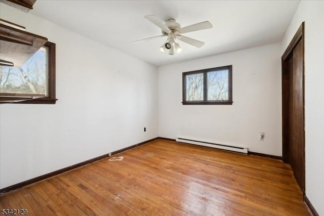 unfurnished bedroom with a baseboard heating unit, ceiling fan, baseboards, and hardwood / wood-style flooring