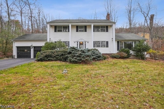 neoclassical / greek revival house with aphalt driveway, a front yard, a chimney, and an attached garage