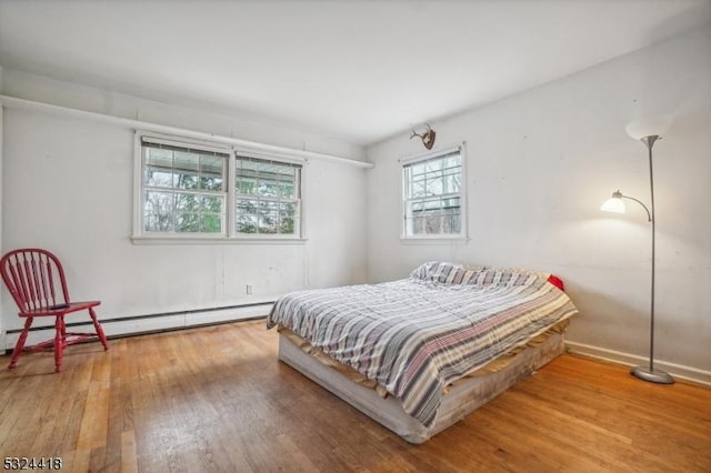 bedroom with a baseboard radiator, wood finished floors, and baseboards