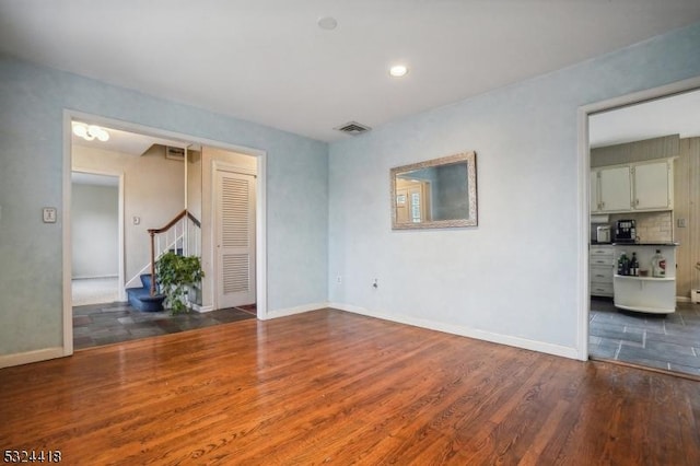 empty room featuring stairs, wood finished floors, visible vents, and baseboards