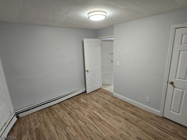 unfurnished room featuring wood finished floors, baseboards, and baseboard heating