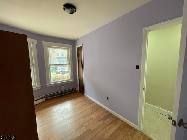 spare room featuring light wood-style floors, a baseboard heating unit, and baseboards