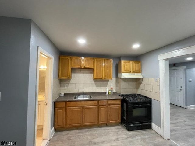 kitchen featuring dark countertops, black gas stove, backsplash, under cabinet range hood, and a sink