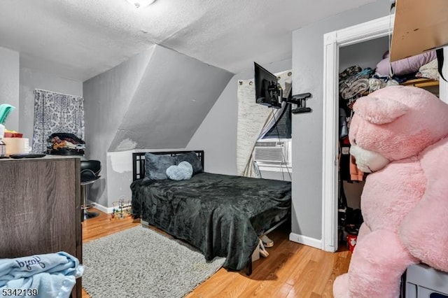 bedroom featuring cooling unit, wood finished floors, baseboards, and a textured ceiling