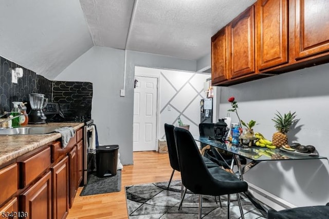 kitchen with light countertops, vaulted ceiling, light wood-style flooring, brown cabinets, and a textured ceiling