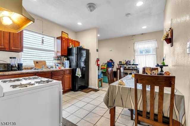 kitchen featuring light tile patterned floors, white range with gas stovetop, freestanding refrigerator, a sink, and wall chimney range hood