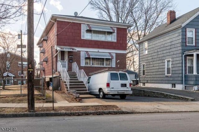 view of front of home featuring concrete driveway, brick siding, and fence