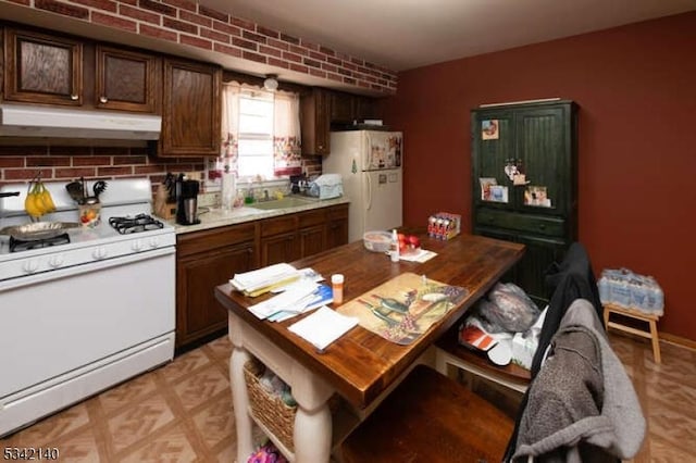 kitchen with light countertops, a sink, brick wall, white appliances, and under cabinet range hood