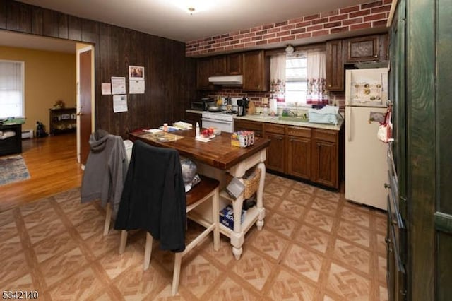 kitchen featuring brick wall, white appliances, wood walls, a sink, and light countertops