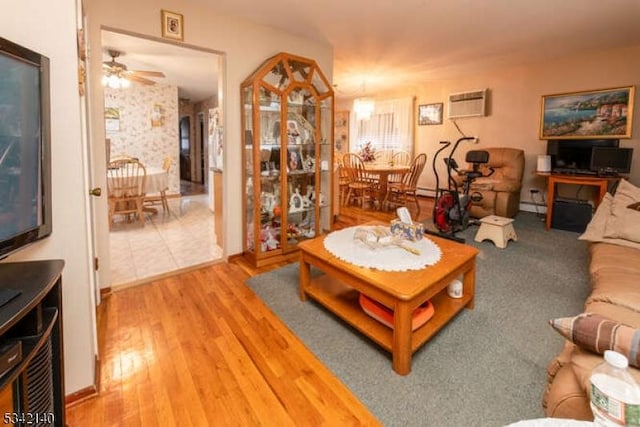 living area with a baseboard heating unit, an AC wall unit, ceiling fan, and wood finished floors