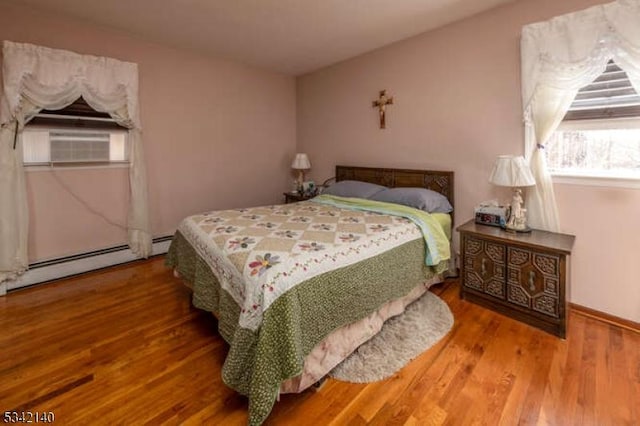 bedroom with a baseboard heating unit, cooling unit, and wood finished floors