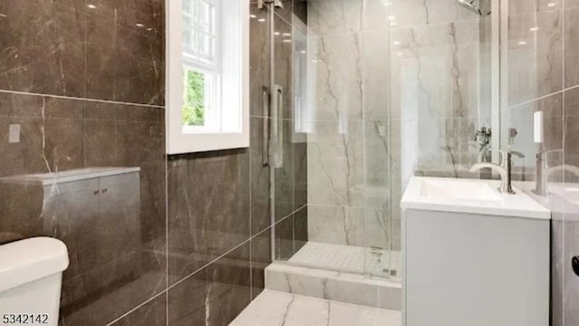 bathroom featuring toilet, a marble finish shower, tile walls, and vanity