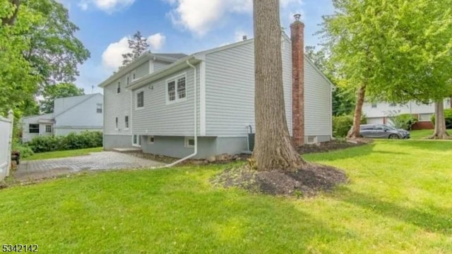 view of home's exterior featuring driveway, a chimney, and a yard