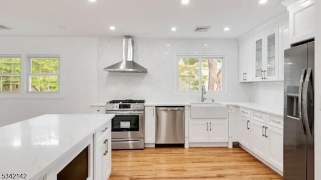 kitchen with stainless steel appliances, white cabinets, a sink, and wall chimney exhaust hood