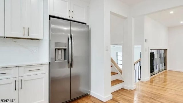 kitchen with stainless steel fridge with ice dispenser, light countertops, light wood-style flooring, white cabinetry, and baseboards