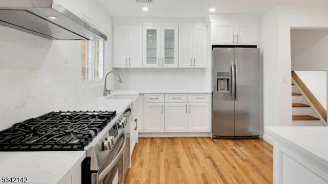 kitchen featuring tasteful backsplash, appliances with stainless steel finishes, white cabinetry, wall chimney range hood, and light wood-type flooring