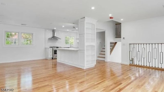 interior space with light wood-type flooring, white cabinets, electric range, and wall chimney exhaust hood