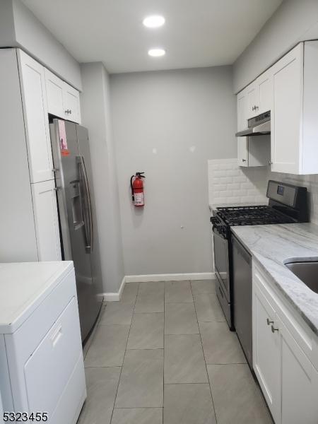 kitchen featuring washer / dryer, stainless steel appliances, under cabinet range hood, white cabinetry, and backsplash