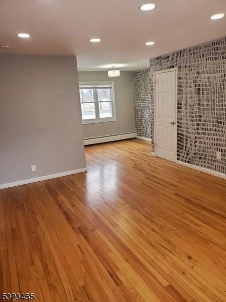 unfurnished room featuring a baseboard radiator, baseboards, wood finished floors, and recessed lighting