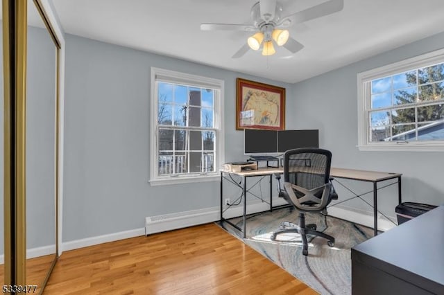 office space with baseboards, baseboard heating, wood finished floors, and a healthy amount of sunlight