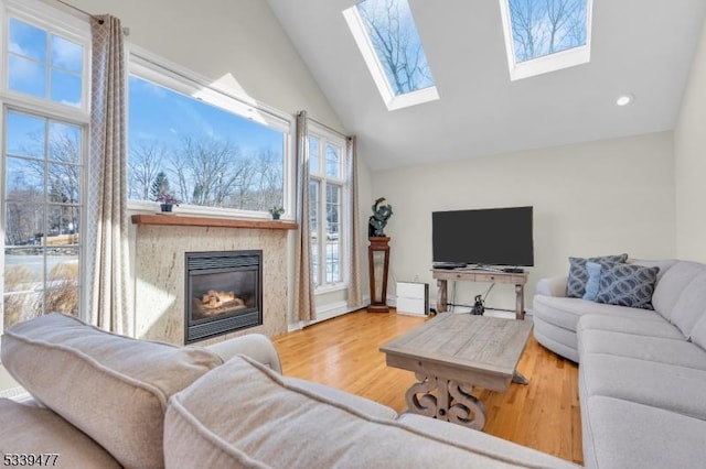 living room featuring a glass covered fireplace, lofted ceiling with skylight, and wood finished floors