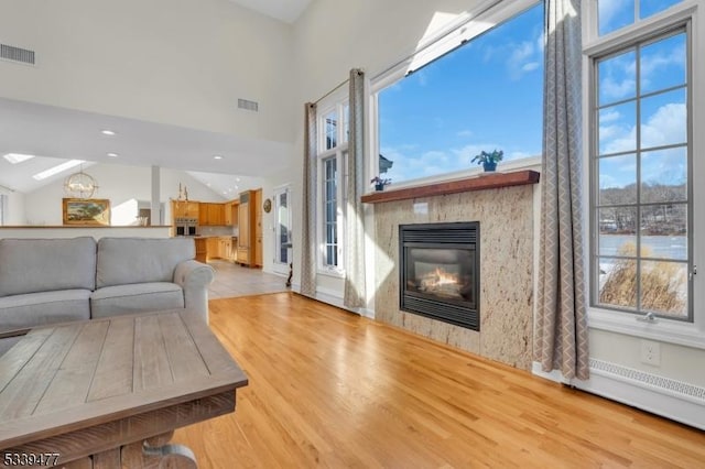 living room featuring light wood-type flooring, a glass covered fireplace, and visible vents