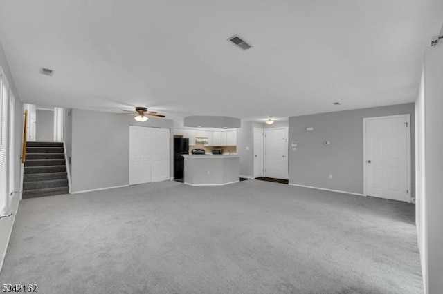 unfurnished living room with baseboards, visible vents, a ceiling fan, light colored carpet, and stairway