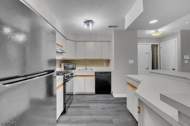 kitchen featuring light countertops, white cabinetry, a sink, under cabinet range hood, and black appliances