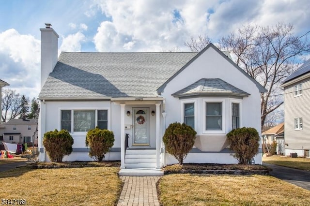 bungalow-style house with roof with shingles, a front lawn, a chimney, and stucco siding