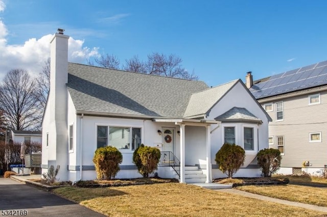 view of front of home featuring roof with shingles, a chimney, a front yard, and stucco siding