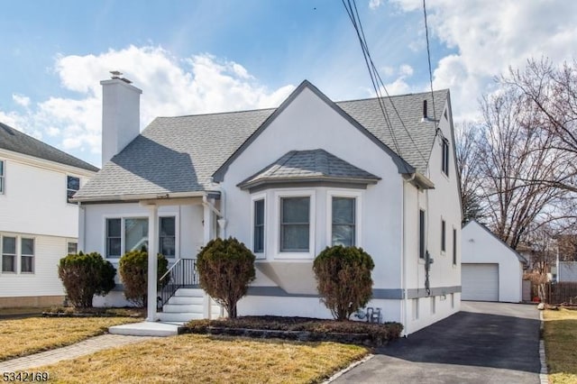 view of front of home with stucco siding, a chimney, roof with shingles, an outdoor structure, and a front yard