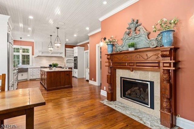 kitchen featuring decorative backsplash, wood-type flooring, ornamental molding, light countertops, and a high end fireplace