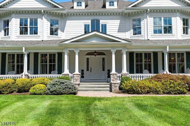 view of front of house featuring roof with shingles, a porch, and a front yard