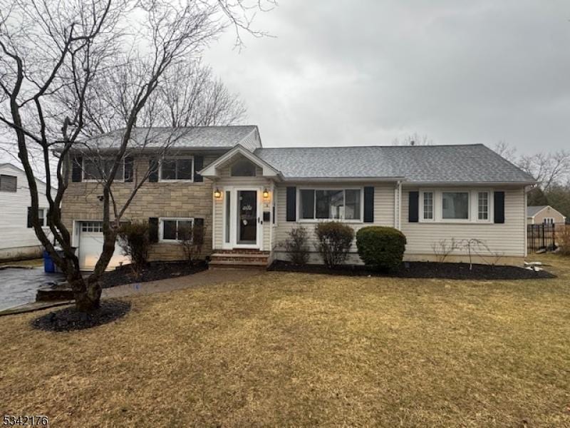 split level home featuring a front yard, stone siding, and fence