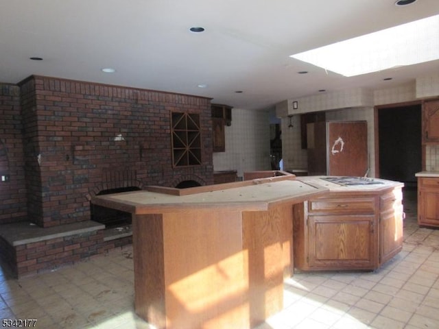 kitchen with a skylight, brown cabinets, cooktop, light countertops, and a kitchen island