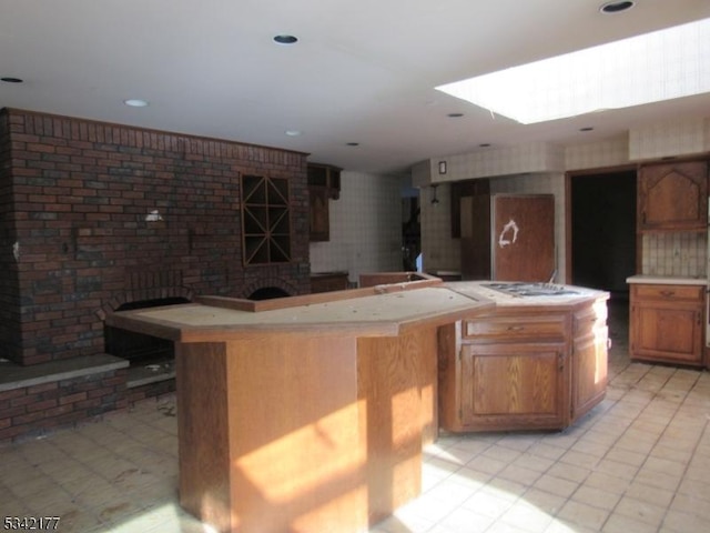 kitchen featuring a fireplace, a skylight, light countertops, brown cabinets, and cooktop