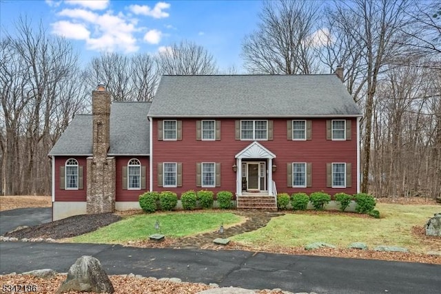 view of front of property with a shingled roof, a chimney, and a front lawn