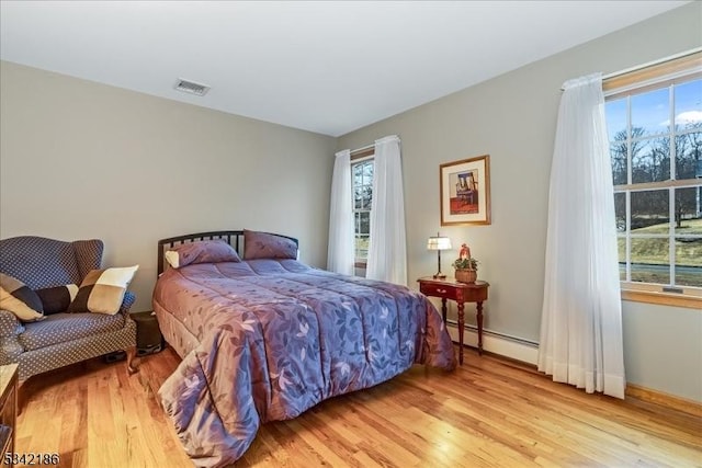 bedroom with light wood-style floors, multiple windows, and a baseboard heating unit